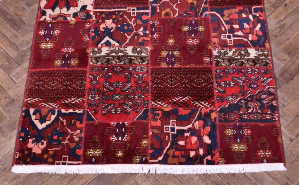 A rectangular hand-stitched Persian patchwork rug featuring geometric and floral panels in deep red, navy blue, and cream with white fringed edges. View II