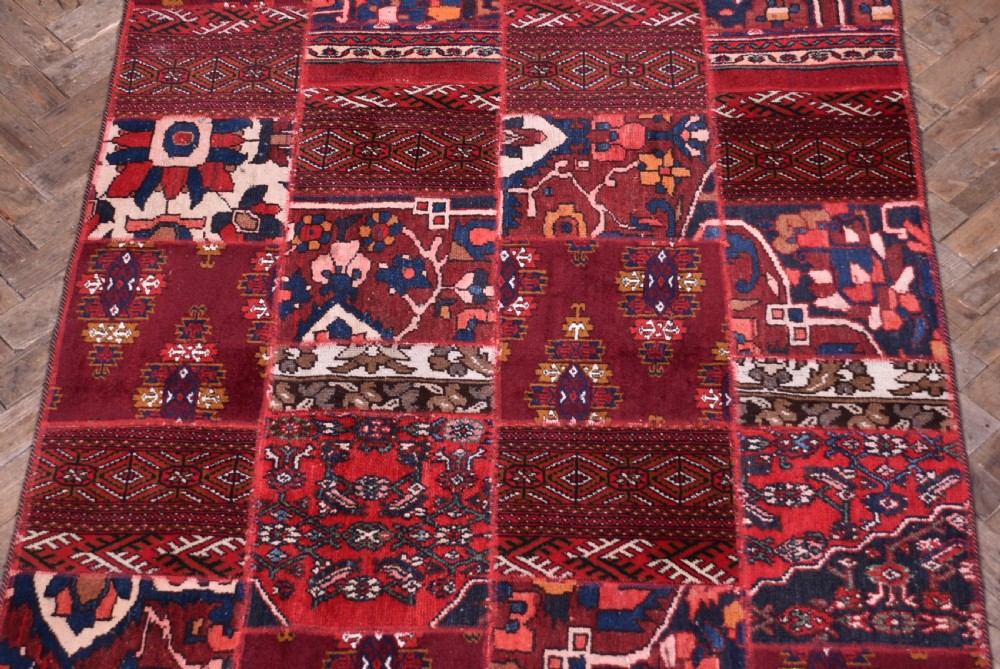 A rectangular hand-stitched Persian patchwork rug featuring geometric and floral panels in deep red, navy blue, and cream with white fringed edges. View III