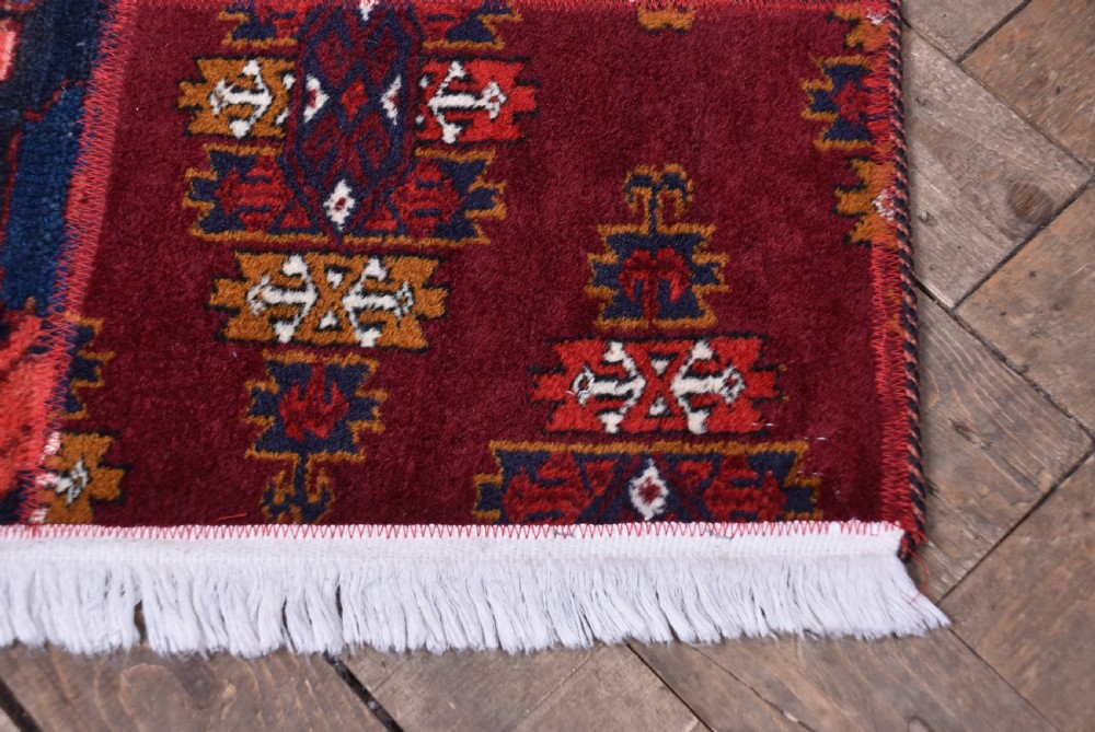 A rectangular hand-stitched Persian patchwork rug featuring geometric and floral panels in deep red, navy blue, and cream with white fringed edges. View V