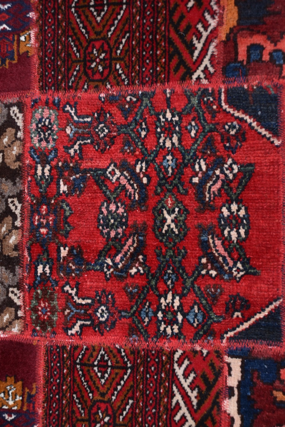 A rectangular hand-stitched Persian patchwork rug featuring geometric and floral panels in deep red, navy blue, and cream with white fringed edges. View VII