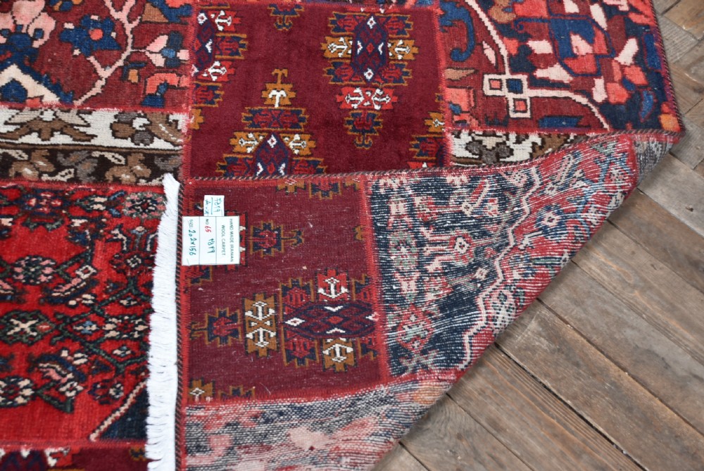 A rectangular hand-stitched Persian patchwork rug featuring geometric and floral panels in deep red, navy blue, and cream with white fringed edges. View VIII