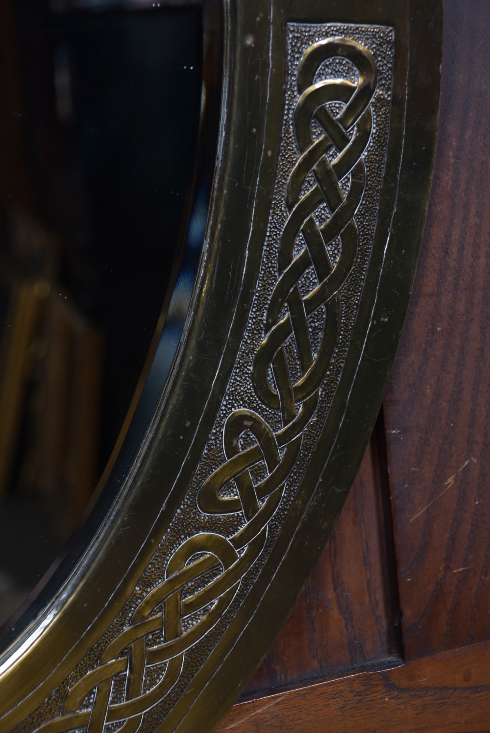 An oval Arts and Crafts brass wall mirror featuring embossed Celtic knotwork interlace detailing around the border frame. View V