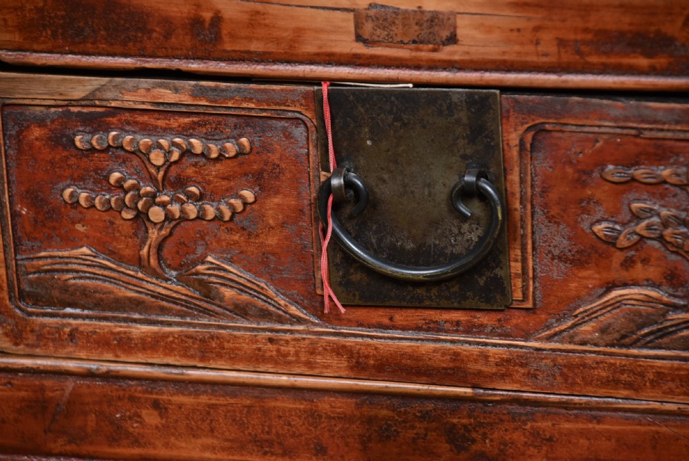 A 19th-century Chinese wooden writing desk featuring carved landscape panels on five drawers, a central openwork fretwork apron, and a warm reddish-brown lacquer finish. View V