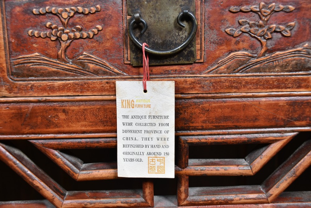 A 19th-century Chinese wooden writing desk featuring carved landscape panels on five drawers, a central openwork fretwork apron, and a warm reddish-brown lacquer finish. View VI