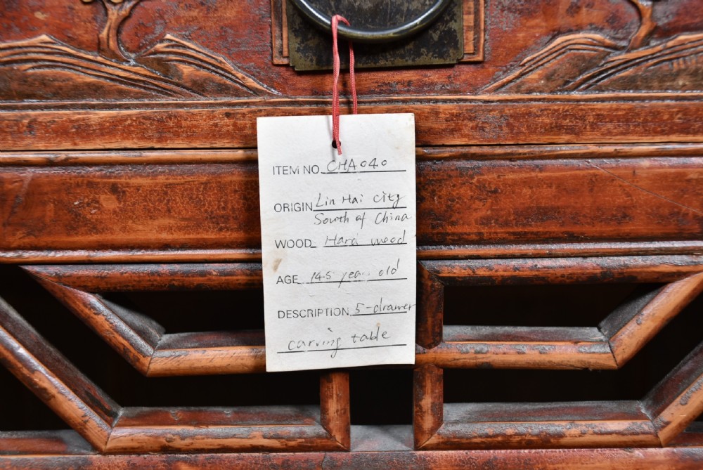 A 19th-century Chinese wooden writing desk featuring carved landscape panels on five drawers, a central openwork fretwork apron, and a warm reddish-brown lacquer finish. View VIII