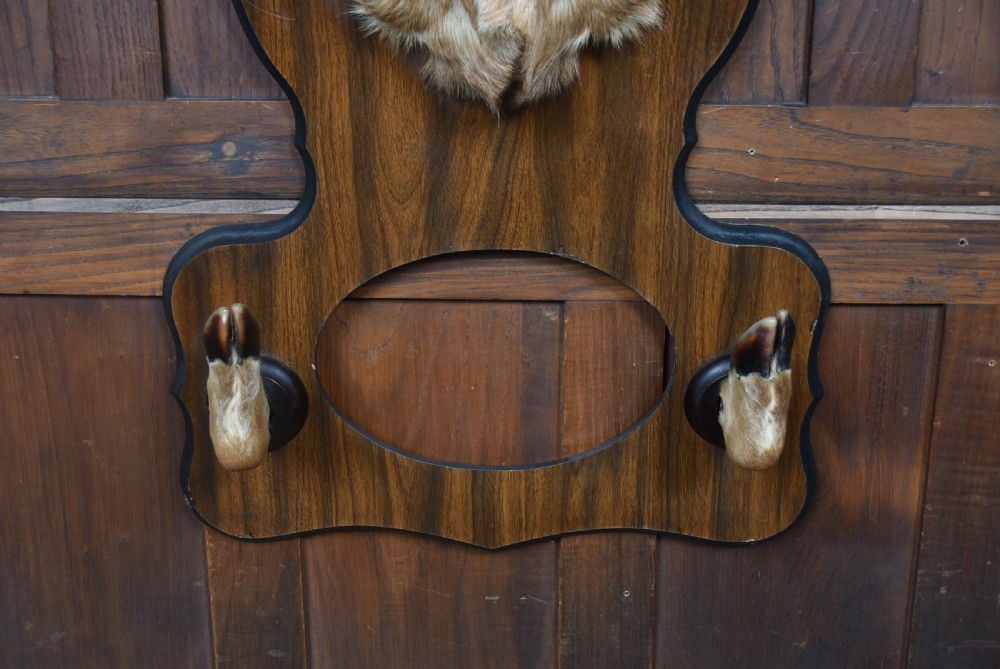A taxidermy whitetail deer shoulder mount mounted on a dark wooden shield-shaped plaque featuring integrated hoof hooks holding a gun. View VI