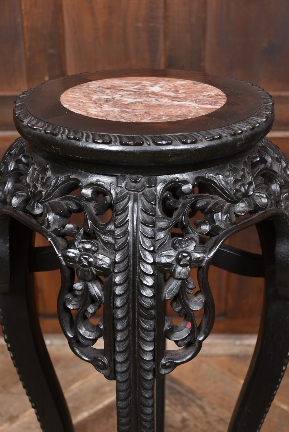 A tall, dark carved hardwood Chinese stand featuring a circular pink marble inset top and an intricate floral pierced apron on cabriole legs. View II