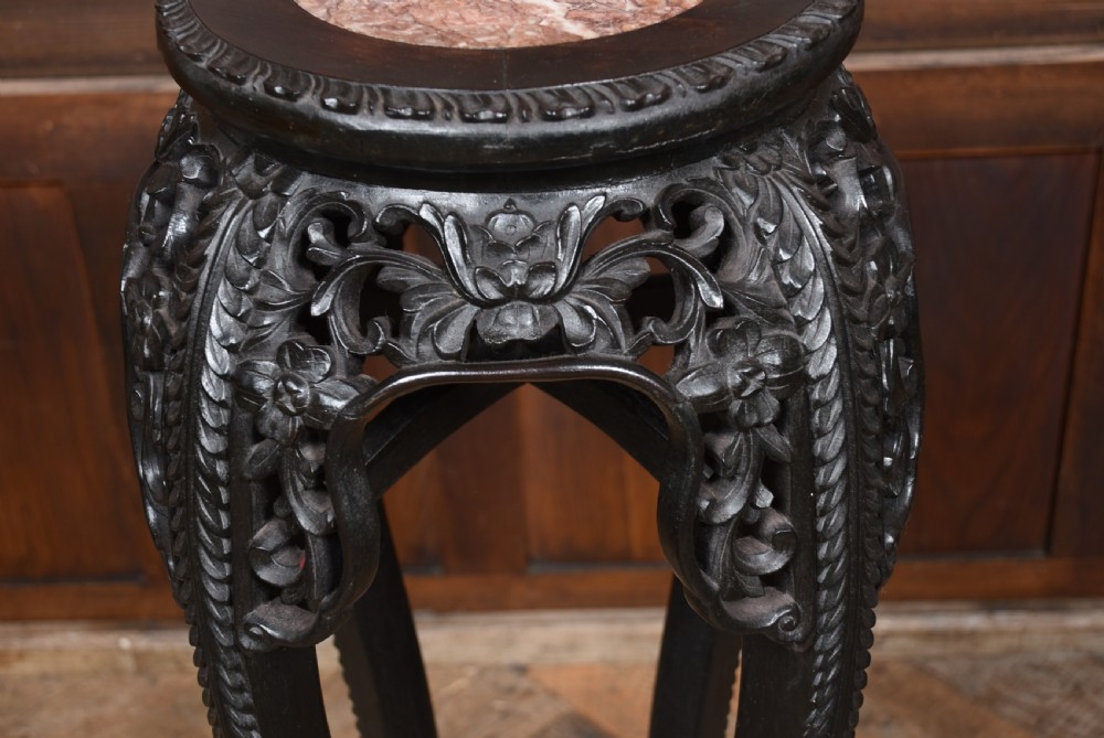 A tall, dark carved hardwood Chinese stand featuring a circular pink marble inset top and an intricate floral pierced apron on cabriole legs. View IV