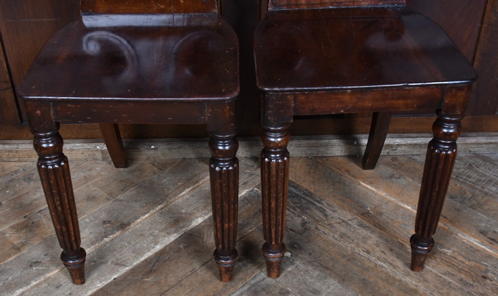 A pair of 19th-century mahogany hall chairs featuring carved scroll backrests, solid wooden seats, and turned fluted front legs. View VIII
