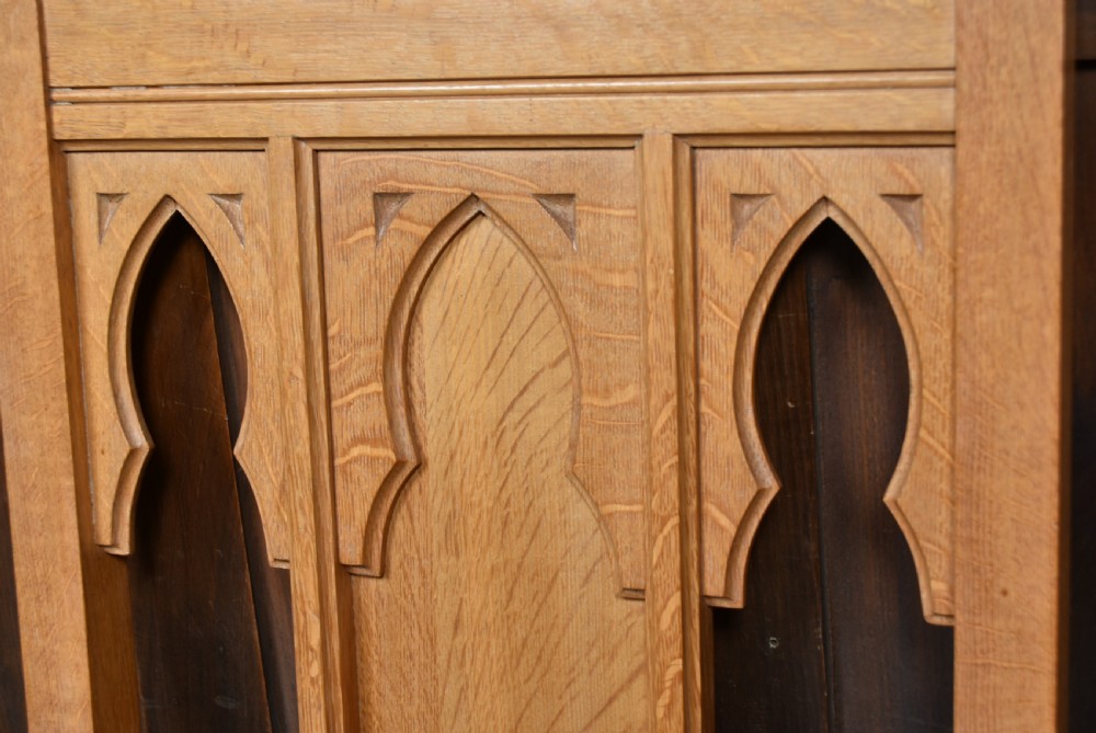A solid oak throne chair featuring a high back decorated with three carved gothic lancet arches, straight armrests, and turned front legs joined by lower stretchers. View VI
