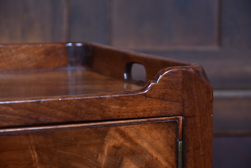 A 19th-century mahogany pot cupboard featuring a single panelled cupboard door with a brass knob, tray top with handles, turned legs, and an X-frame stretcher. View IV