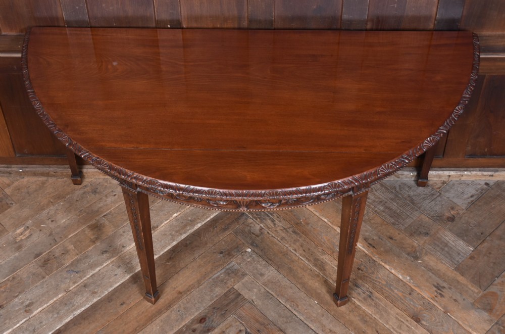 A pair of demilune mahogany console tables featuring carved friezes with swag motifs and four square tapered legs. View VI