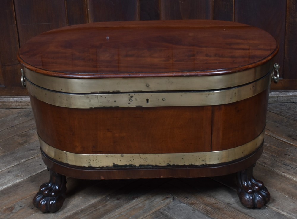 An oval 19th-century mahogany cellarette featuring brass bands, side handles, and carved lion paw feet.