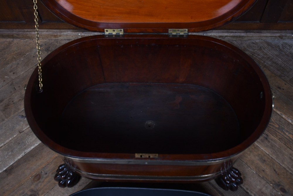 An oval 19th-century mahogany cellarette featuring brass bands, side handles, and carved lion paw feet. View V