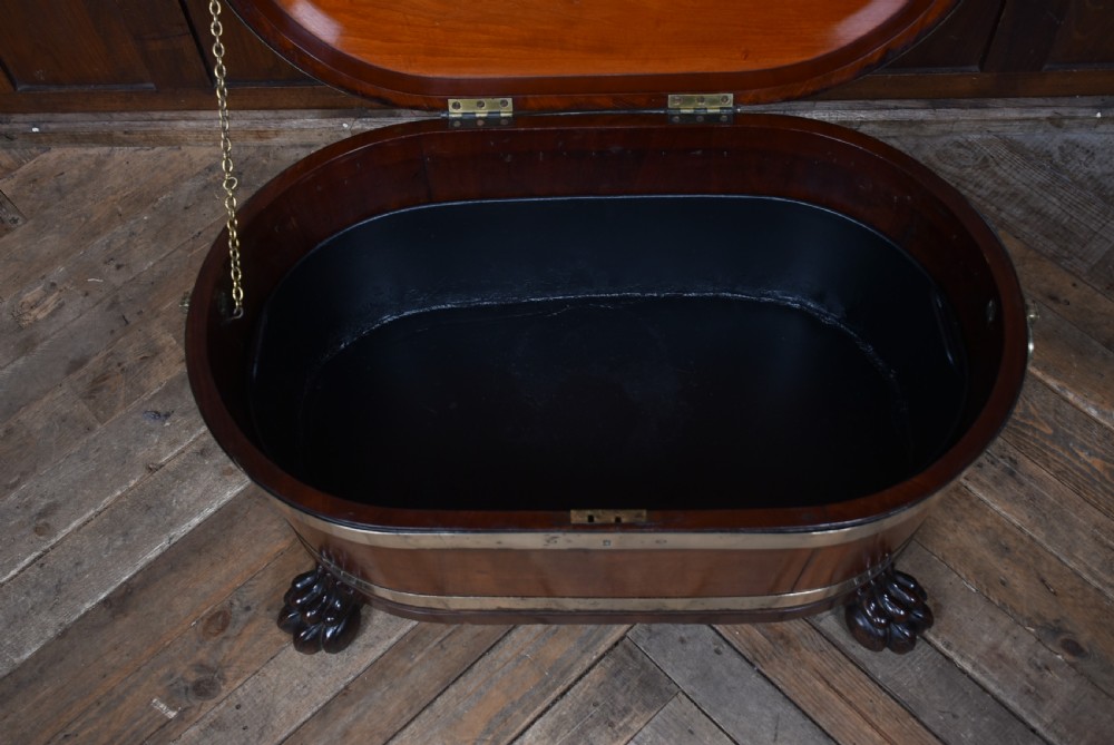 An oval 19th-century mahogany cellarette featuring brass bands, side handles, and carved lion paw feet. View VI