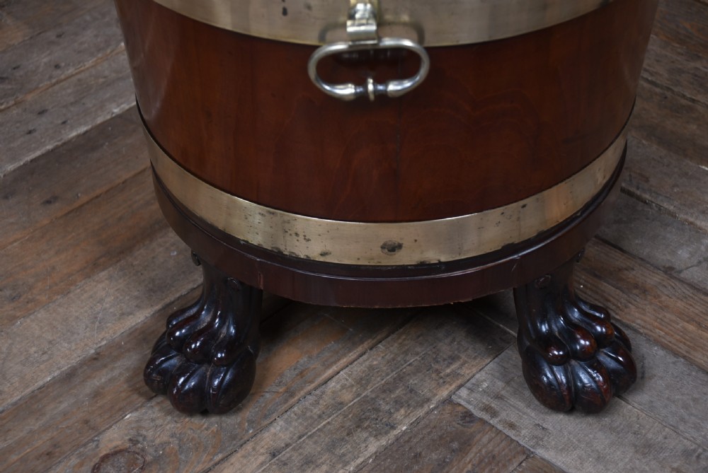 An oval 19th-century mahogany cellarette featuring brass bands, side handles, and carved lion paw feet. View IX