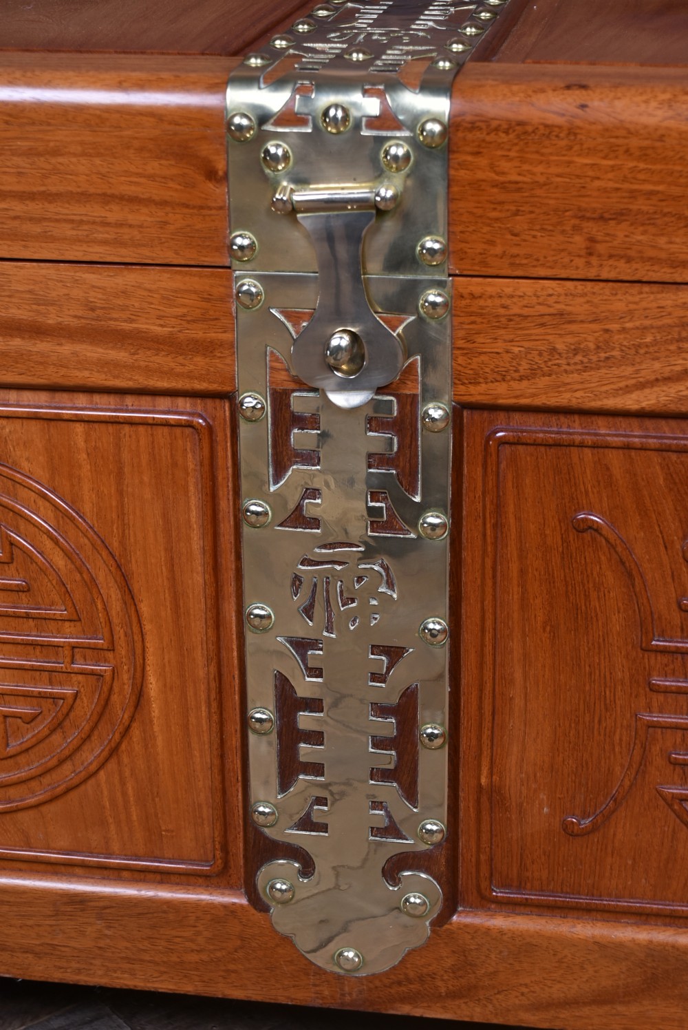 A rectangular reddish brown timber blanket box featuring carved Chinese character panels and polished brass corner fittings and straps. View VI