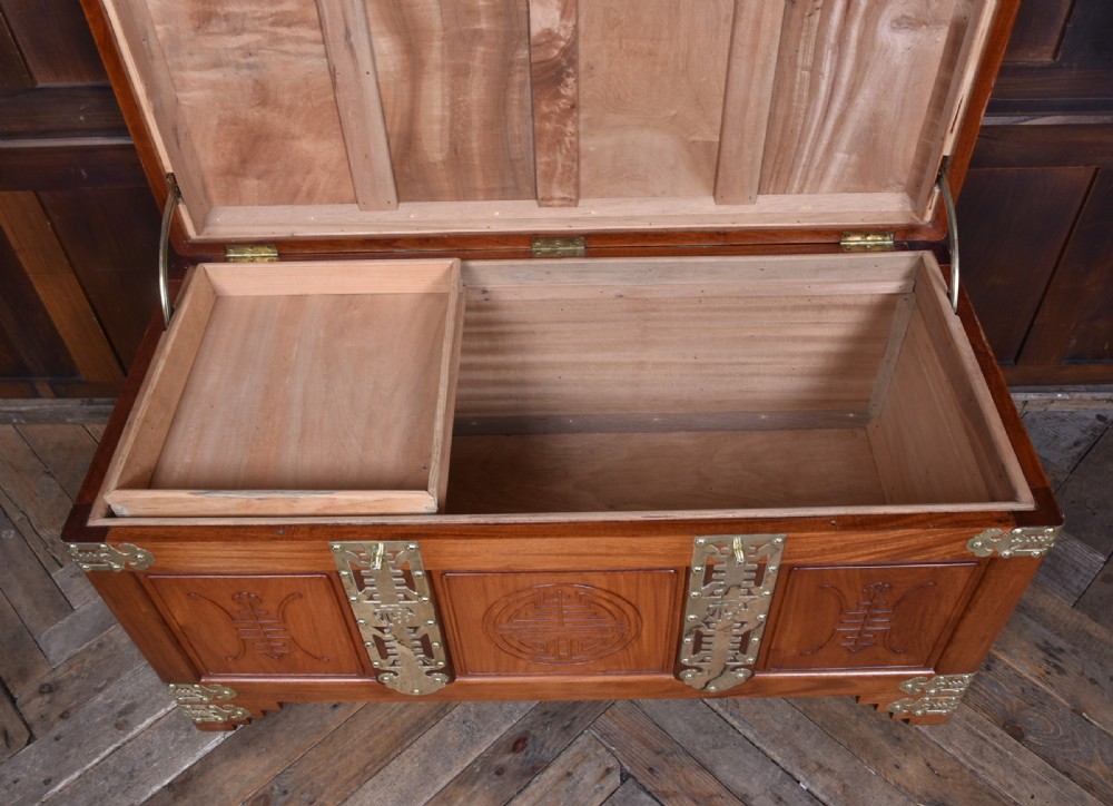 A rectangular reddish brown timber blanket box featuring carved Chinese character panels and polished brass corner fittings and straps. View XI