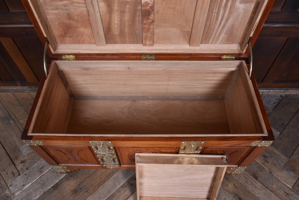 A rectangular reddish brown timber blanket box featuring carved Chinese character panels and polished brass corner fittings and straps. View XIII