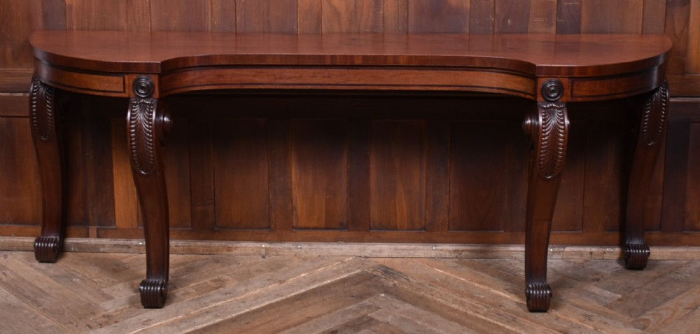 A 19th-century mahogany console table featuring a shaped top, inlaid frieze, and four carved scroll legs.