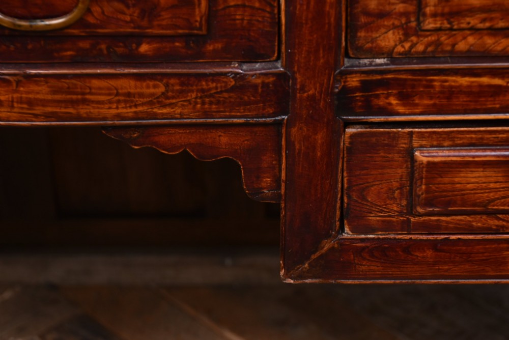 A traditional Chinese warm brown hardwood partners desk featuring six front drawers with brass drop handles and square legs. View IV