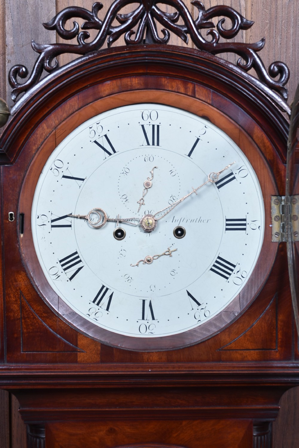 An antique Scottish flame mahogany longcase clock featuring a carved swan-neck pediment with brass finials, a rounded dial, and a veneered trunk door. View II