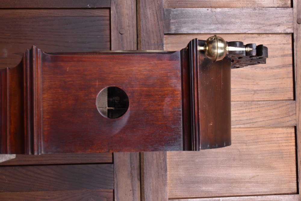 An antique Scottish flame mahogany longcase clock featuring a carved swan-neck pediment with brass finials, a rounded dial, and a veneered trunk door. View V