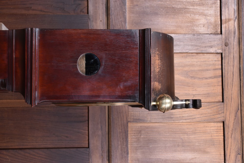 An antique Scottish flame mahogany longcase clock featuring a carved swan-neck pediment with brass finials, a rounded dial, and a veneered trunk door. View VI