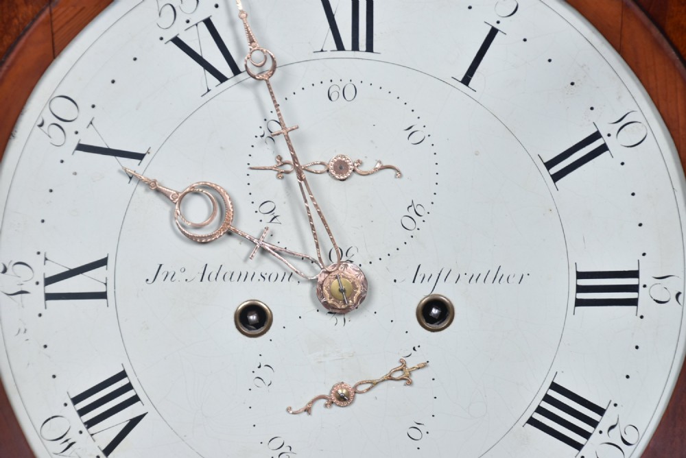 An antique Scottish flame mahogany longcase clock featuring a carved swan-neck pediment with brass finials, a rounded dial, and a veneered trunk door. View X