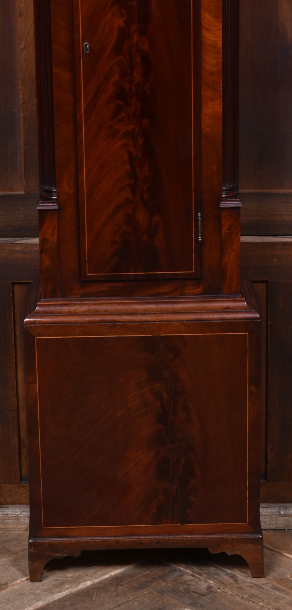 An antique Scottish flame mahogany longcase clock featuring a carved swan-neck pediment with brass finials, a rounded dial, and a veneered trunk door. View XV
