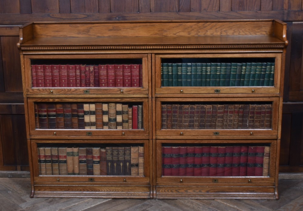 An Edwardian golden oak six-section bookcase featuring double columns of glass-fronted lifting doors and brass hardware.