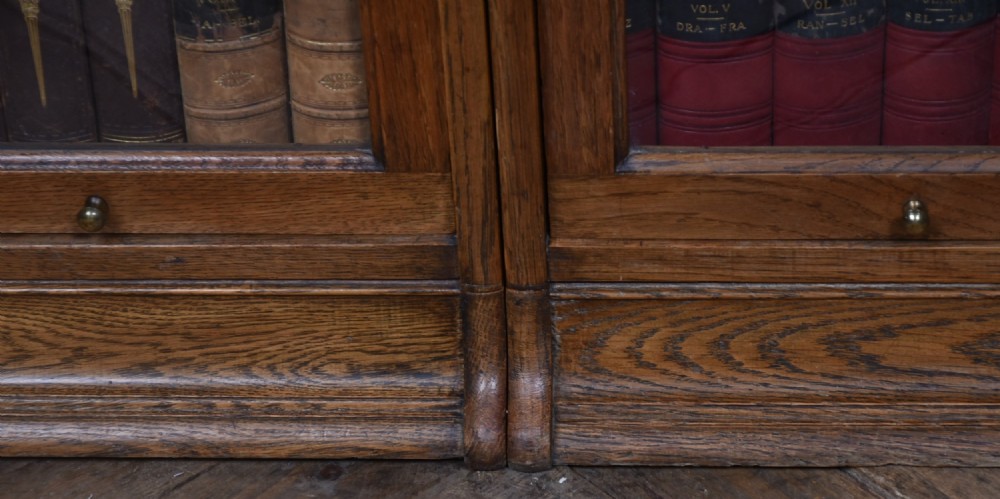 An Edwardian golden oak six-section bookcase featuring double columns of glass-fronted lifting doors and brass hardware. View V