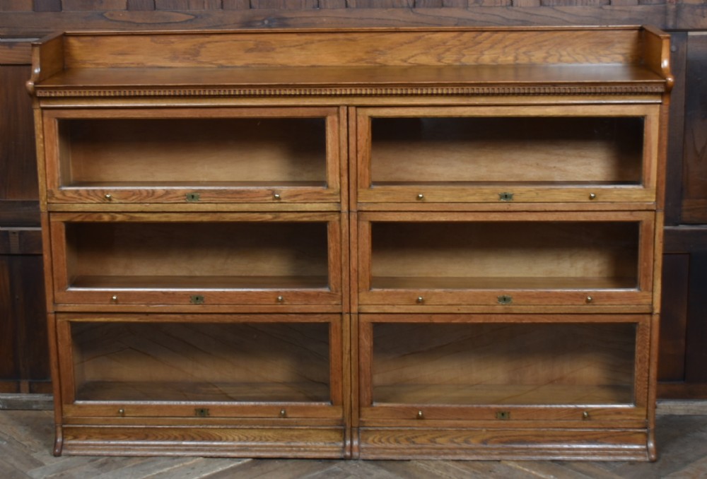 An Edwardian golden oak six-section bookcase featuring double columns of glass-fronted lifting doors and brass hardware. View VI