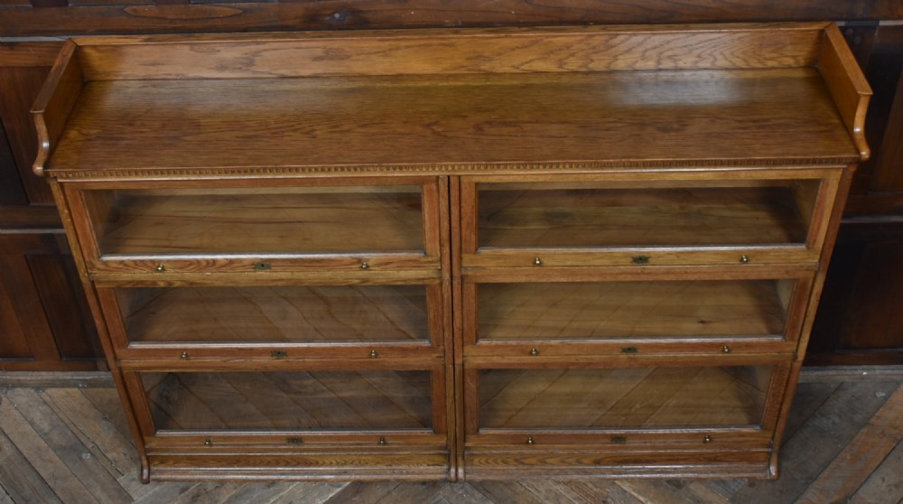 An Edwardian golden oak six-section bookcase featuring double columns of glass-fronted lifting doors and brass hardware. View VII