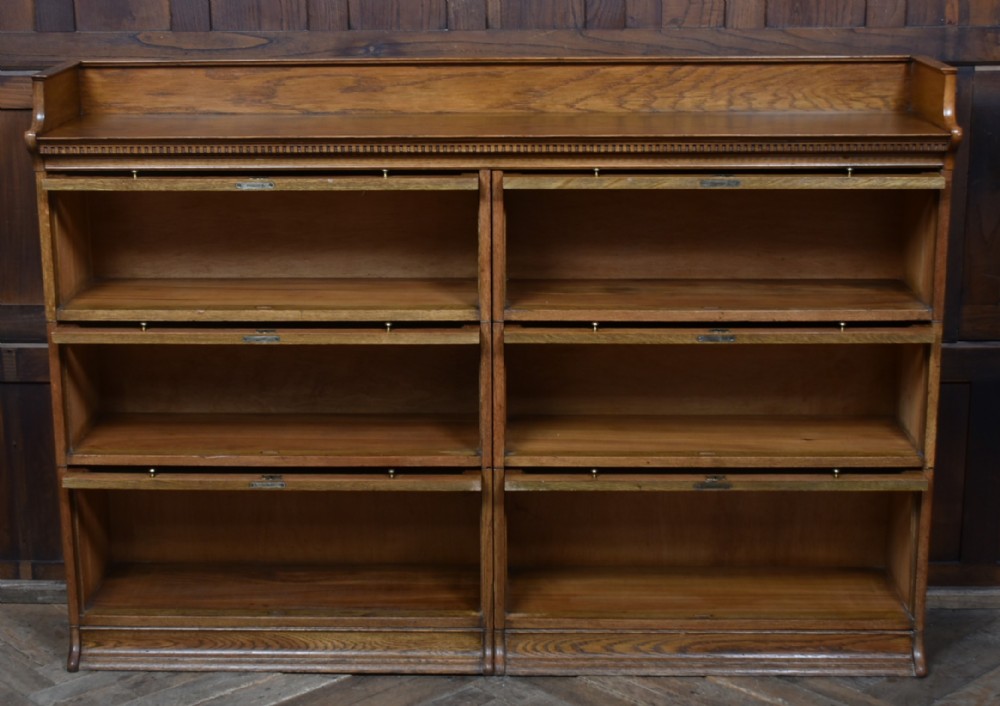 An Edwardian golden oak six-section bookcase featuring double columns of glass-fronted lifting doors and brass hardware. View X