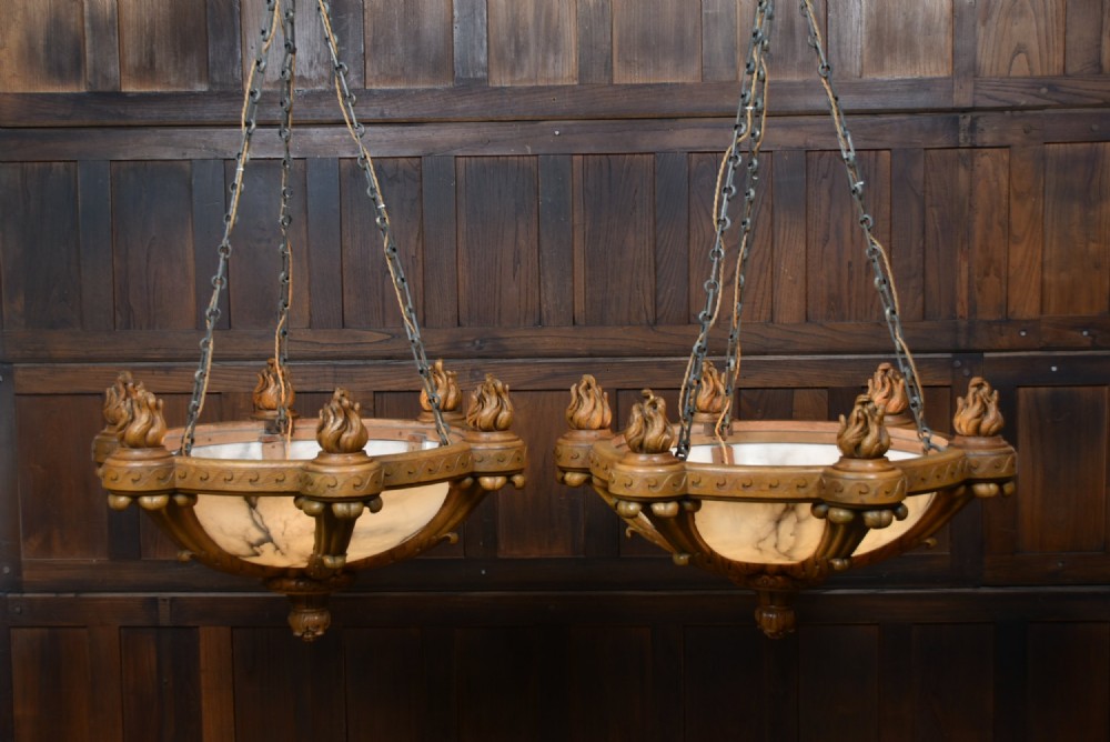 A pair of Art Deco ceiling lights featuring translucent veined alabaster bowls encased in carved wooden rims with flame finials and metal chains.