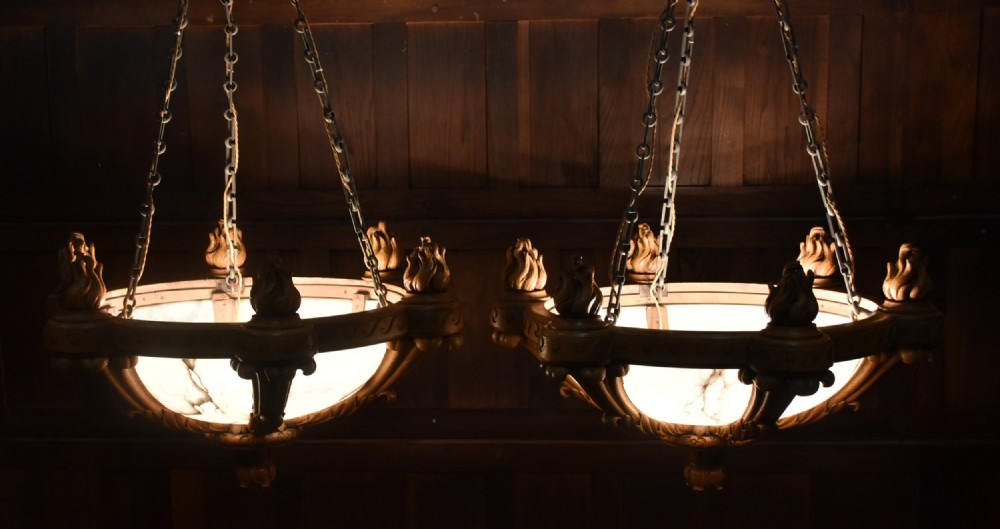 A pair of Art Deco ceiling lights featuring translucent veined alabaster bowls encased in carved wooden rims with flame finials and metal chains. View III