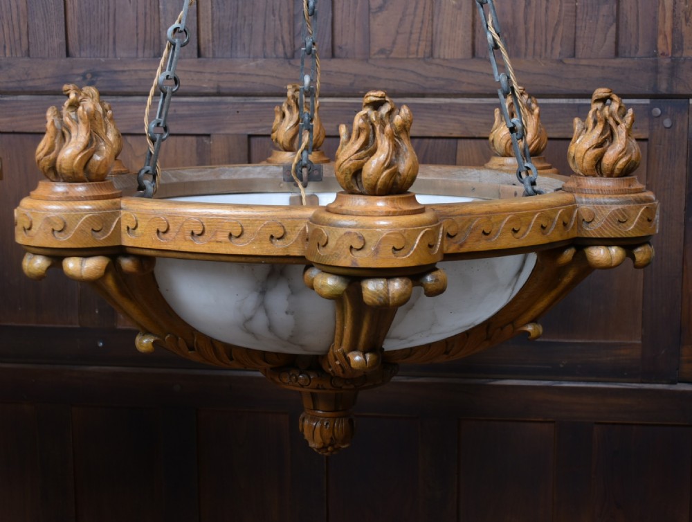 A pair of Art Deco ceiling lights featuring translucent veined alabaster bowls encased in carved wooden rims with flame finials and metal chains. View X