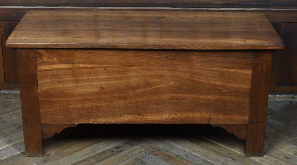 An antique French cherrywood blanket box with a hinged rectangular lid, natural wood grain, and shaped corner apron. View II