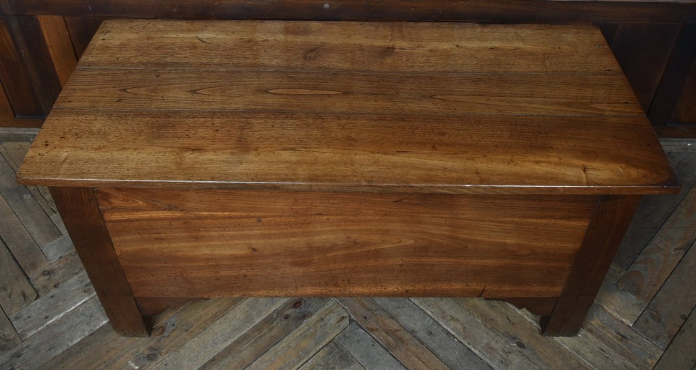An antique French cherrywood blanket box with a hinged rectangular lid, natural wood grain, and shaped corner apron. View III