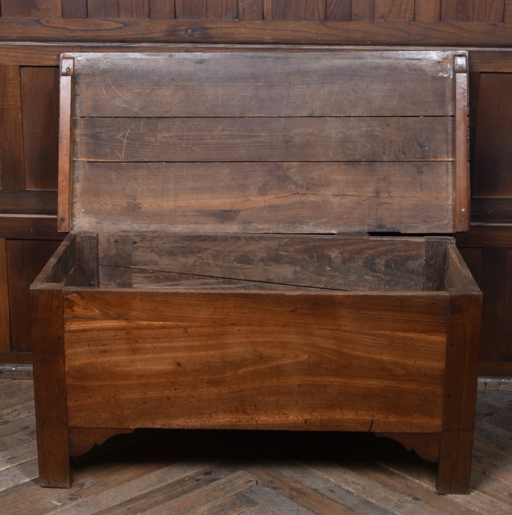 An antique French cherrywood blanket box with a hinged rectangular lid, natural wood grain, and shaped corner apron. View IV