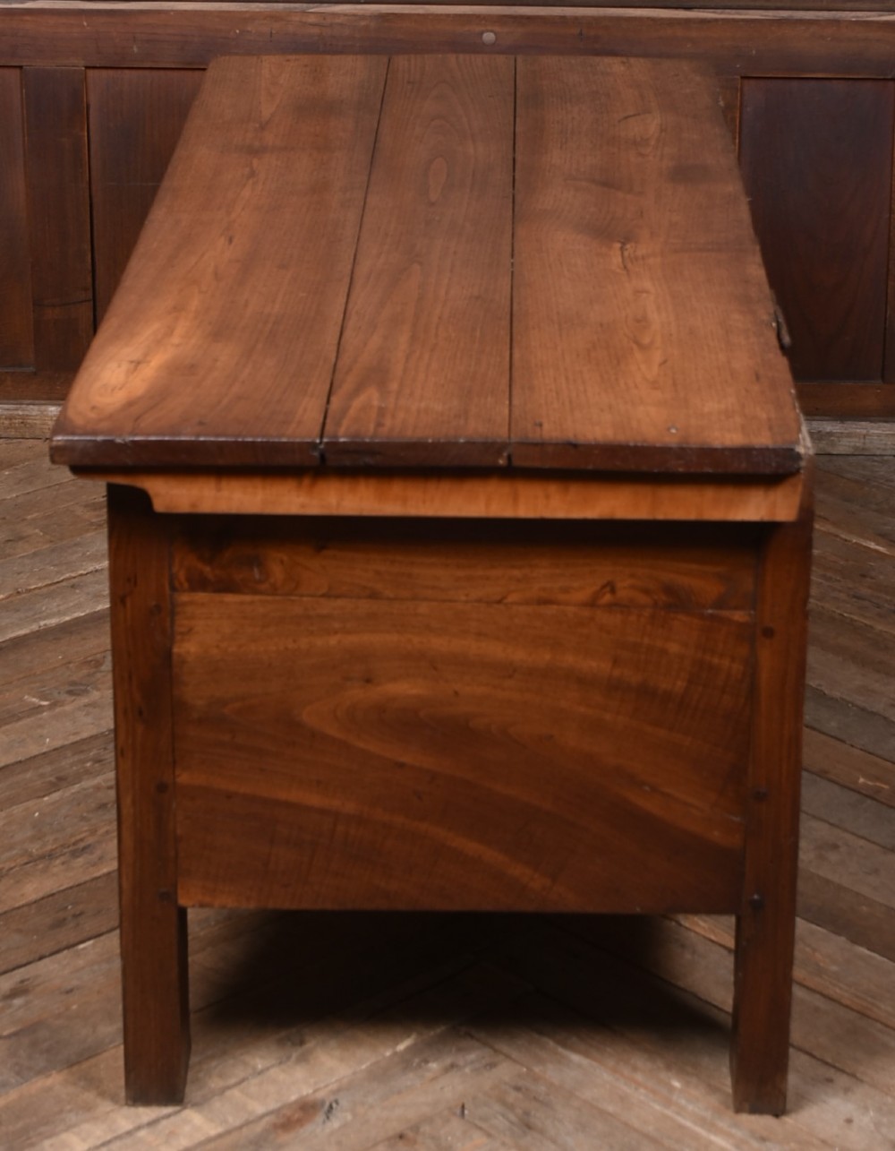 An antique French cherrywood blanket box with a hinged rectangular lid, natural wood grain, and shaped corner apron. View VIII
