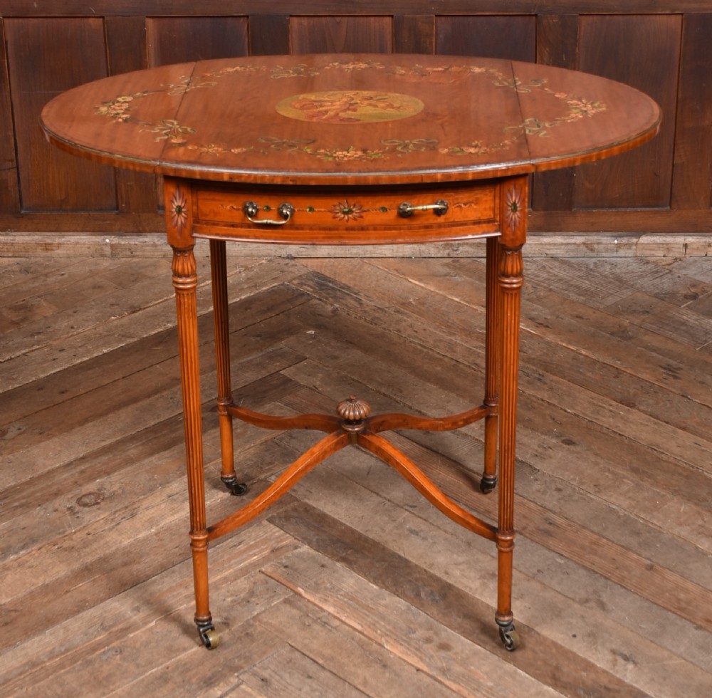 An Edwardian Neoclassical drop-leaf table featuring hand-painted floral swags, a central figural medallion, fluted turned legs, and an X-stretcher on castors.