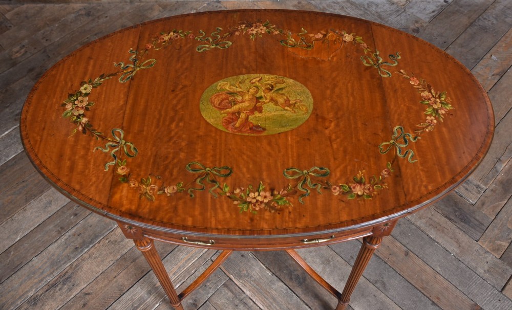 An Edwardian Neoclassical drop-leaf table featuring hand-painted floral swags, a central figural medallion, fluted turned legs, and an X-stretcher on castors. View III