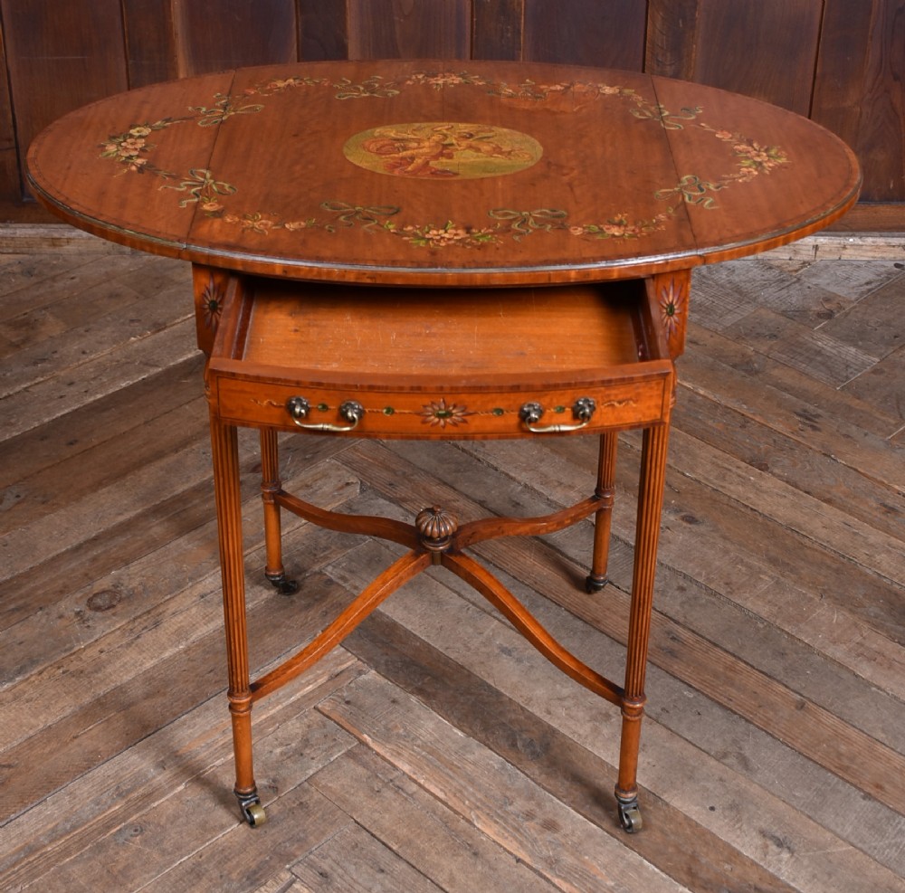 An Edwardian Neoclassical drop-leaf table featuring hand-painted floral swags, a central figural medallion, fluted turned legs, and an X-stretcher on castors. View IV
