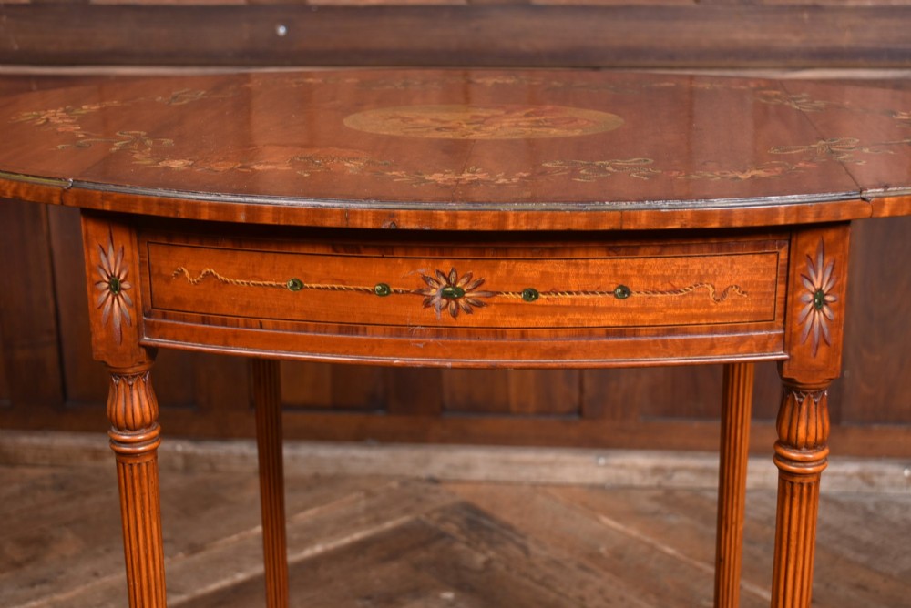 An Edwardian Neoclassical drop-leaf table featuring hand-painted floral swags, a central figural medallion, fluted turned legs, and an X-stretcher on castors. View VI