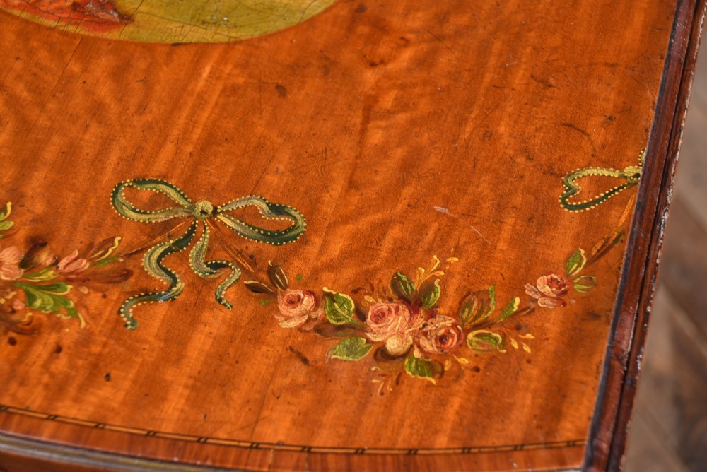 An Edwardian Neoclassical drop-leaf table featuring hand-painted floral swags, a central figural medallion, fluted turned legs, and an X-stretcher on castors. View IX
