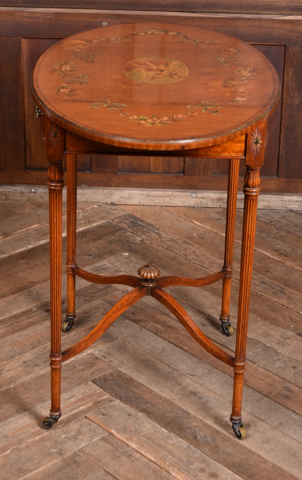 An Edwardian Neoclassical drop-leaf table featuring hand-painted floral swags, a central figural medallion, fluted turned legs, and an X-stretcher on castors. View XIV