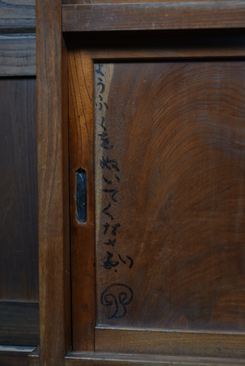 A tall wooden Japanese Mizuya tansu cabinet featuring multiple sliding door compartments, small drawers with iron drop handles, and faint calligraphic inscriptions on an upper panel. View II