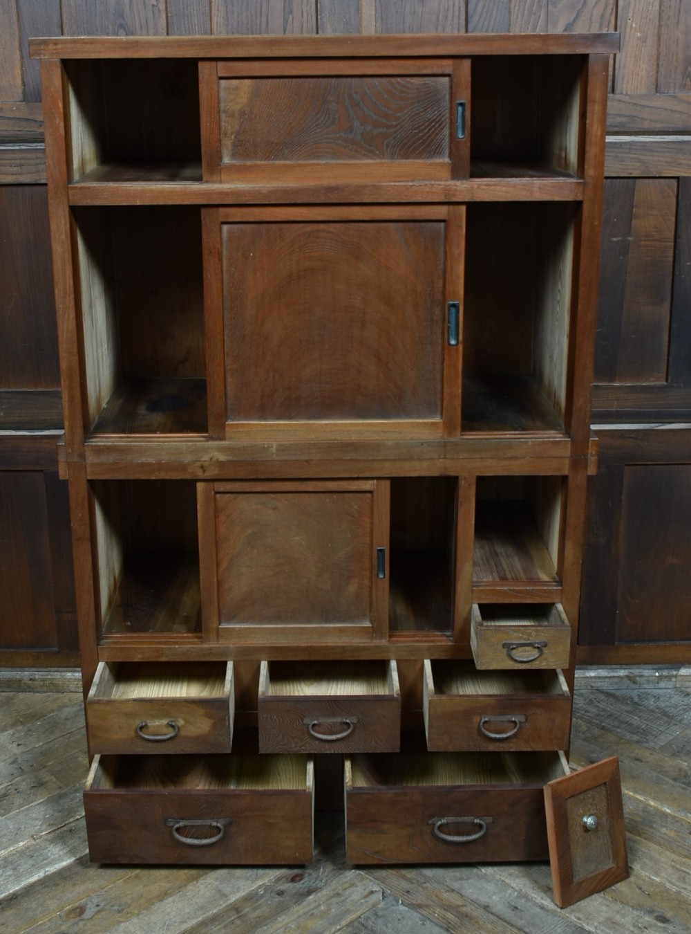 A tall wooden Japanese Mizuya tansu cabinet featuring multiple sliding door compartments, small drawers with iron drop handles, and faint calligraphic inscriptions on an upper panel. View IV
